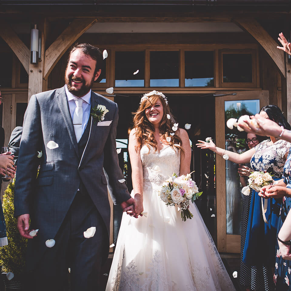 The bride and groom step outside to guests throwing confetti at their summer wedding
