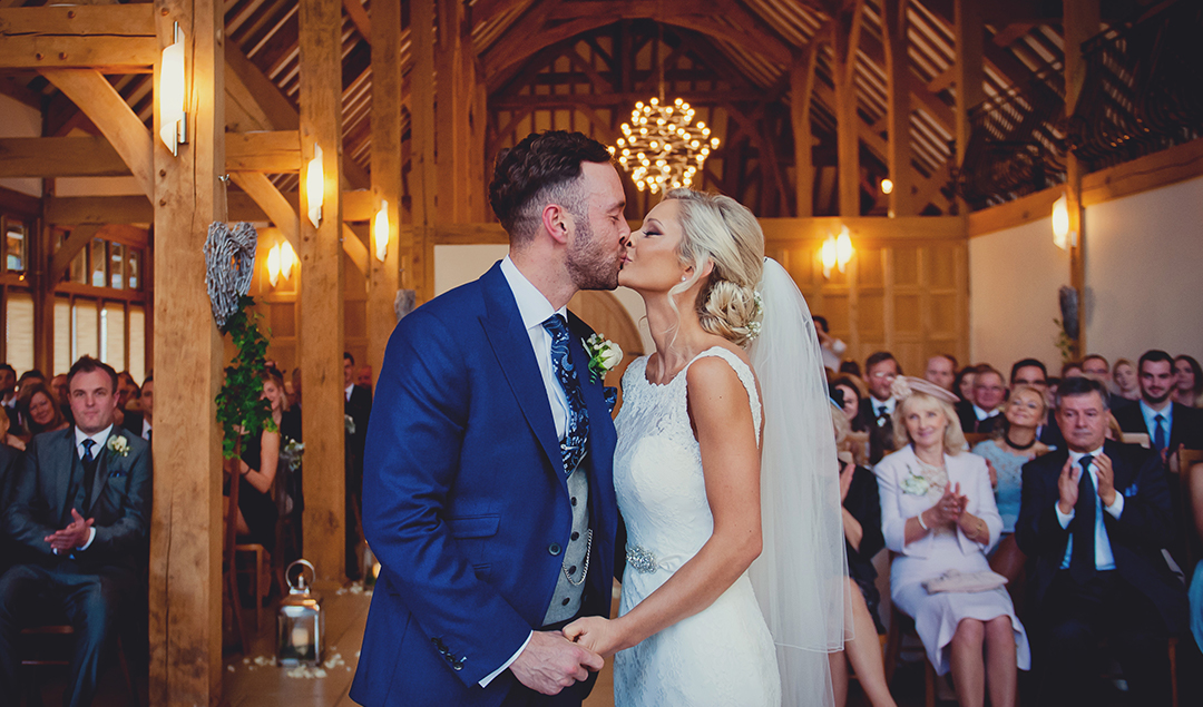 The bride and groom share a kiss at their wedding ceremony in this beautiful barn venue