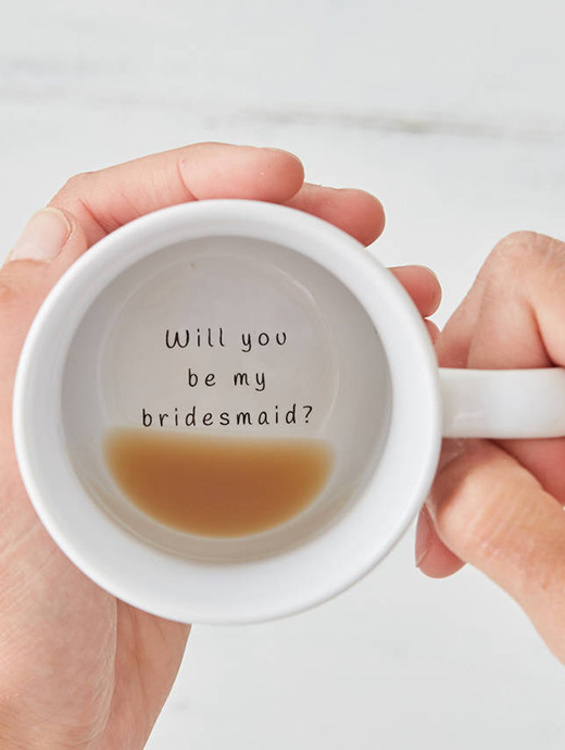 A finished cup of tea with “will you be my bridesmaid” wrote at the bottom of the mug