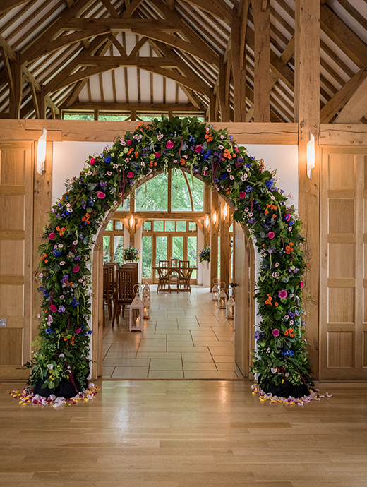 A beautifully full wedding arch filled with bright colours makes up the entrance this Hampshire barn wedding venue