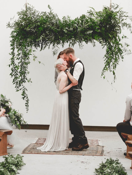 newlyweds sharing a kiss under a hanging wedding DIY wedding arch