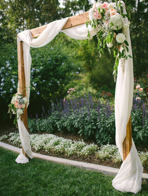 An outdoor wedding arch made from wood and wrapped in white linen and florals