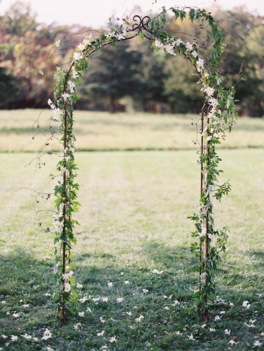 a simple and delicate metal framed wedding arch covered in baby pink flowers and green leaves