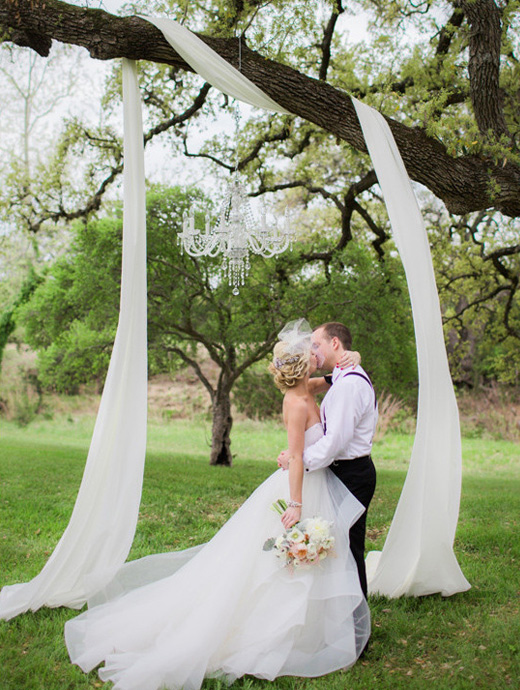 A couple sharing a kiss under a simple DIY wedding arch hanging from a tree